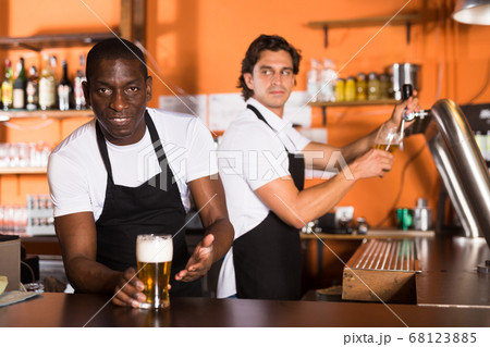 Smiling man bartender offering glass of golden beer in bar Smiling man bartender offering glass of golden beer in bar 68123885