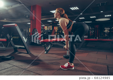 Young muscular caucasian woman practicing in gym with equipment. Wellness, healthy lifestyle, bodybuilding. Young muscular caucasian woman practicing in gym with equipment. Wellness, healthy lifestyle, bodybuilding. 68124985