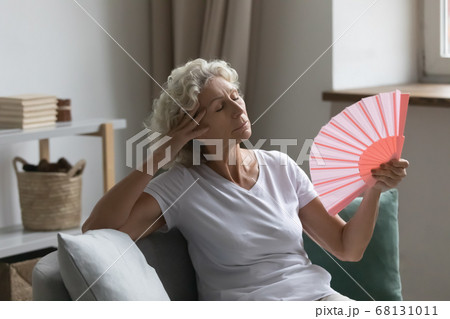 Senior woman waving fan feels unwell due unbearable hot weather Senior woman waving fan feels unwell due unbearable hot weather 68131011