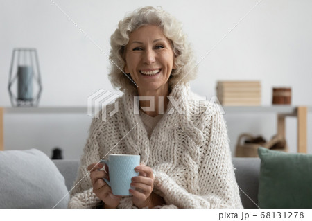 Senior woman holding cup relaxing on couch wrapped in plaid 68131278