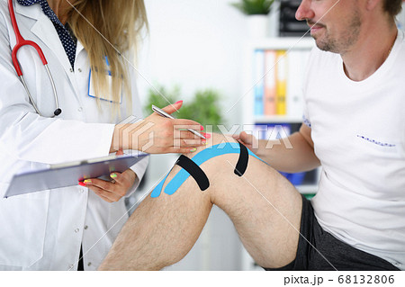Doctor examines an injured knee in patient with kinesio tape Doctor examines an injured knee in patient with kinesio tape 68132806