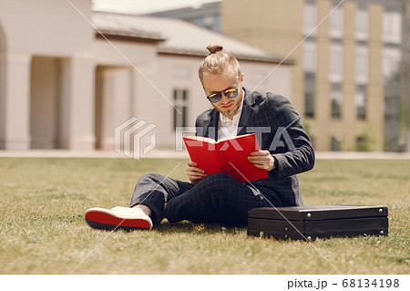Businessman with book sitting in a summer city 68134198