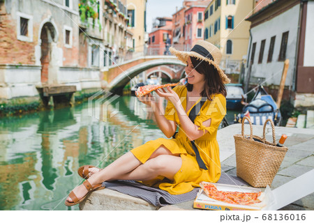 woman sitting on pond with view of venice canal eating pizza 68136016