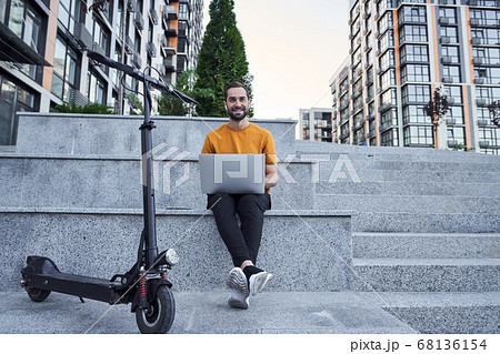 Happy young rider using laptop on stairs outdoors 68136154