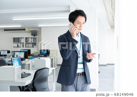 早朝1人でオフィスに出社して電話する不安顔の若いビジネスマン 早朝1人でオフィスに出社して電話する不安顔の若いビジネスマン 68149046