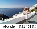 Female In a white dress posing against the backdrop of the city of Thira, Santorini. 68149568