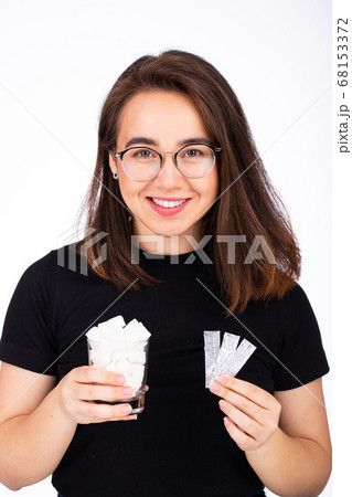young beautiful woman in glasses with a smile, holds in one hand a glass of white sugar, in the other hand a plate of chewing gum 68153372