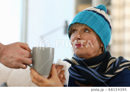The grandmother sits on the couch and holds a cup The grandmother sits on the couch and holds a cup 68154395