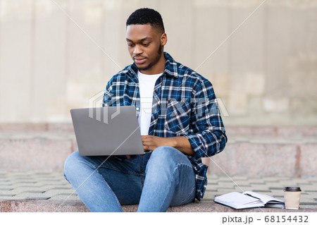 Student using laptop, sitting on the border in city 68154432