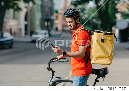 Modern mobile applications. Young man in helmet, with bag, on bicycle looks at smartphone 68154747