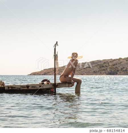 View of unrecognizable woman wearing big summer sun hat tanning topless and relaxing on old wooden pier in remote calm cove of Adriatic sea, Croatia View of unrecognizable woman wearing big summer sun hat tanning topless and relaxing on old wooden pier in remote calm cove of Adriatic sea, Croatia 68154814