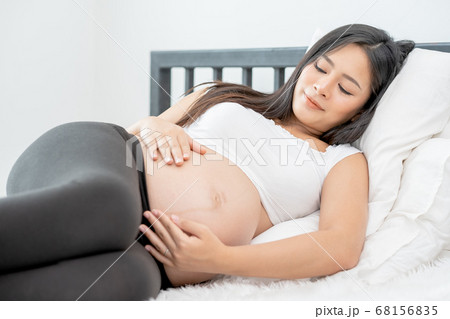 Beautiful Asian pregnant woman lie on bed and use two hands touch belly Beautiful Asian pregnant woman lie on bed and use two hands touch belly 68156835
