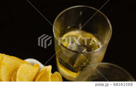 glass of whiskey with ice cubes and salty snacks 68161509