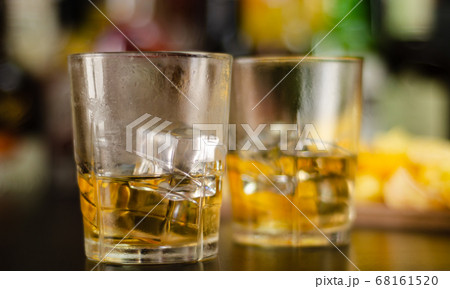 glass of whiskey with ice cubes and salty snacks 68161520