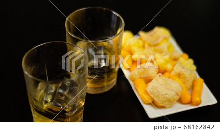 glass of whiskey with ice cubes and salty snacks 68162842
