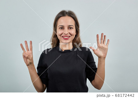 woman in black t-shirt gray background, happy smiling girl shows eight fingers 68172442