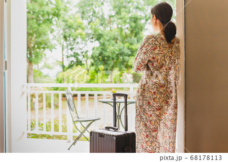 Tourist woman standing near window looking at beautiful garden view with her luggage in hotel bedroom. 68178113