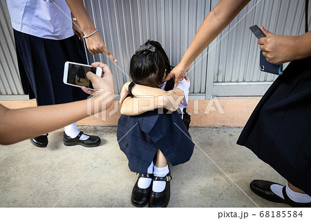 Problems of bullying at school,sad stressed asian girl student crying sitting on the floor,group of hands pointing finger to scared schoolgirl, bullying victim being video recorded on a mobile phone  68185584
