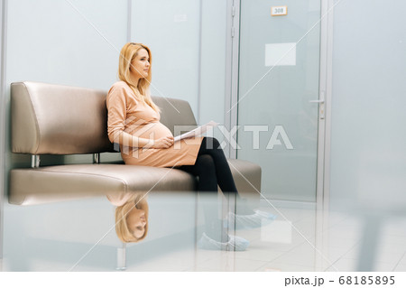 Serious young pregnant woman is sitting in hallway of hospital waiting to see gynecologist. 68185895