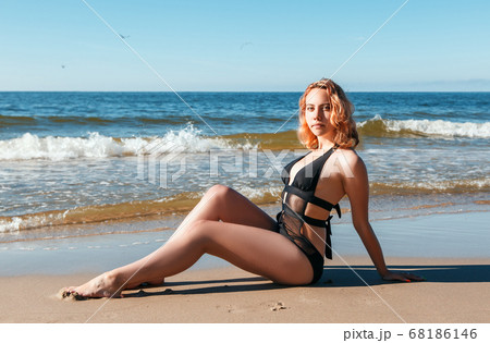 young blonde girl in a black swimsuit sits on the sand of the sea shore young blonde girl in a black swimsuit sits on the sand of the sea shore 68186146