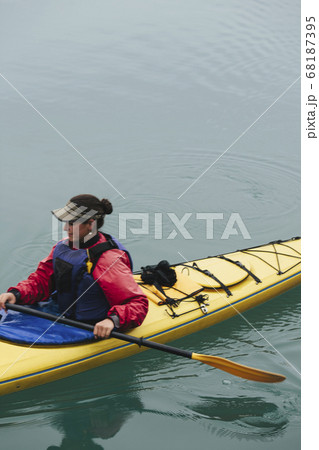 Female sea kayaker paddling pristine waters of Muir Inlet, overcast sky in distance, Glacier Bay National Park, Alaska 68187395
