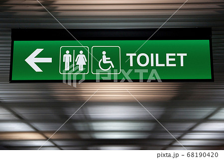 green restroom or toilet sign with arrow hang from ceiling at public area 68190420