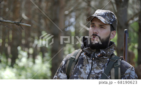Portrait of handsome young man hunter or tourist. Man in camouflage clothes hunts outdoor in forest hunting alone. Close up of man hiker standing in forest. Hunter hunts down prey. Portrait of handsome young man hunter or tourist. Man in camouflage clothes hunts outdoor in forest hunting alone. Close up of man hiker standing in forest. Hunter hunts down prey. 68190623