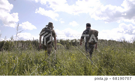 Fishermen go fishing. Relaxed men spending leisure together and going for fishing on river. View from back of walking men in camouflage with fishing rods. Fishermen go fishing. Relaxed men spending leisure together and going for fishing on river. View from back of walking men in camouflage with fishing rods. 68190707