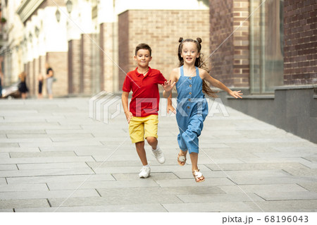 Two smiling kids, boy and girl running together in town, city in summer day Two smiling kids, boy and girl running together in town, city in summer day 68196043