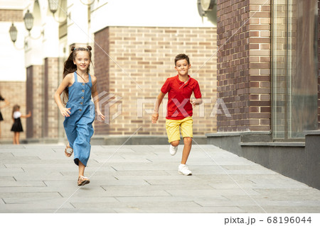 Two smiling kids, boy and girl running together in town, city in summer day Two smiling kids, boy and girl running together in town, city in summer day 68196044