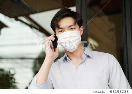 フェースマスクの男性がカフェの前で携帯電話で連絡を取っている 68198288