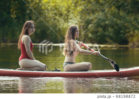 Two women sailing on the inflatable boat on river and using a paddle Two women sailing on the inflatable boat on river and using a paddle 68198872