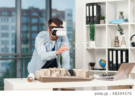 Skillful male architect reviewing architectural project with vr goggles at modern office. 68204370