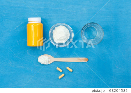 Powder for preparing the solution, a jar for pills, and a glass of water on a blue background. top view, horizontal 68204582