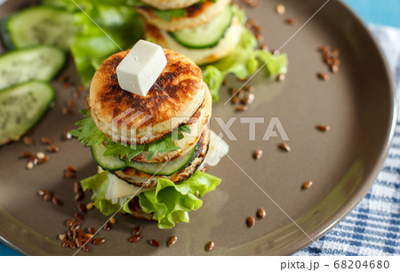 plate with a sandwich of small pancakes with salad and cheese on a wooden table, top view 68204680