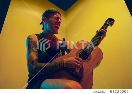 Young caucasian musician inspired performing on yellow background in neon light 68229005