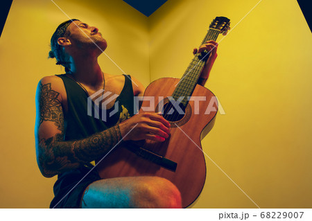 Young caucasian musician inspired performing on yellow background in neon light 68229007