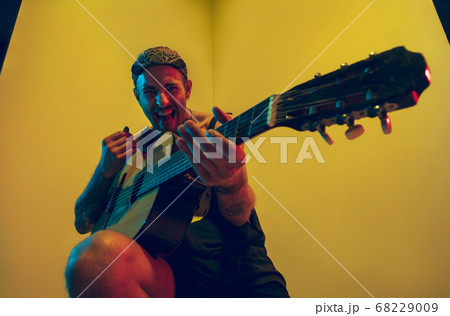 Young caucasian musician inspired performing on yellow background in neon light 68229009