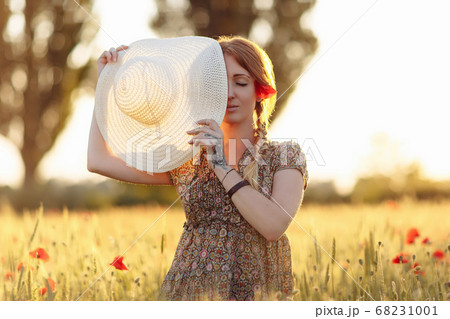 Redhead woman with hat on green field with poppies Redhead woman with hat on green field with poppies 68231001