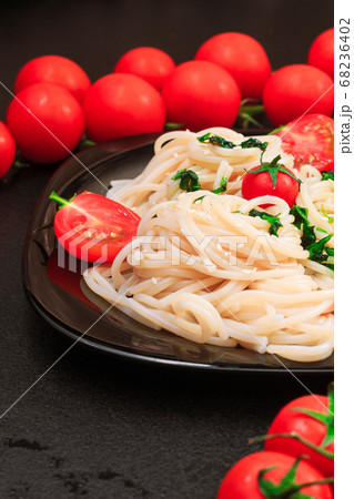 spaghetti with spinach, tomatoes, sesame seeds on a black table on a black plate. close up, copy space 68236402