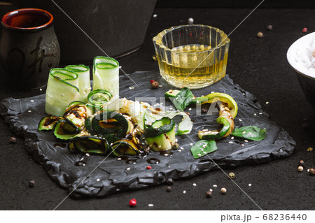 Grilled zucchini with sauce and cucumber, sesame seeds on a black table, close up 68236440
