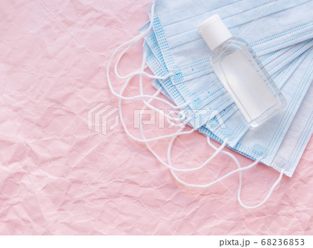 Top view on pack of blue protective medical masks and transparent bottle of sanitizer gel. Coronavirus COVID-19 concept on pink crumpled background with copy space. 68236853