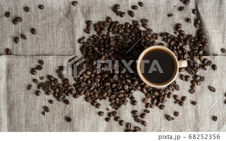 Coffee cup with roasted coffee beans on linen background. Mug of black coffe with scattered coffee beans. Fresh coffee beans. Coffee cup with roasted coffee beans on linen background. Mug of black coffe with scattered coffee beans. Fresh coffee beans. 68252356