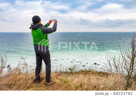 Hiker in green rain jacket takes photos by phone Hiker in green rain jacket takes photos by phone 68253782