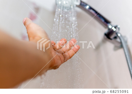 hands check the temperature of the shower water. a man's hand under a stream of water selective focus 68255091