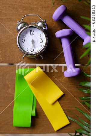 Alarm clock and women dumbbells lying on wooden table. Alarm clock and women dumbbells lying on wooden table. 68258215
