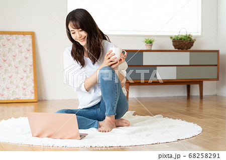 リビングで立て膝をついてノートパソコンを見る若い女性 68258291
