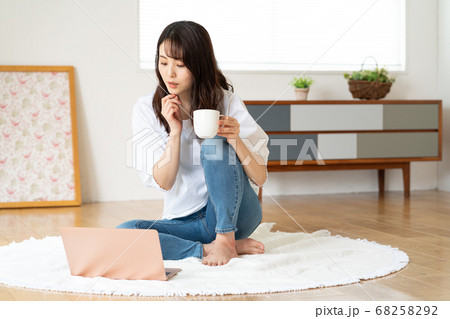 リビングで立て膝をついて動画を鑑賞する若い女性 68258292