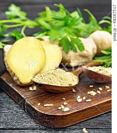 Ginger ground and flakes in spoons on black wood 68267517