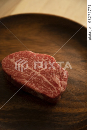 木の机の上のアカシアプレートに乗せた生の肉厚牛フィレステーキ 68272771